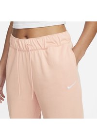 Gaiši rozā Nike sporta bikses ar elastīgu jostasvietu, ar aukliņu un mazu baltu logotipu kreisajā pusē. Gluda tekstūra.