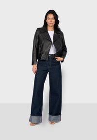 Veste en cuir noir avec quincaillerie argentée, associée à un pantalon en denim foncé taille haute à jambes larges avec un ourlet contrastant. Un simple top blanc en dessous.