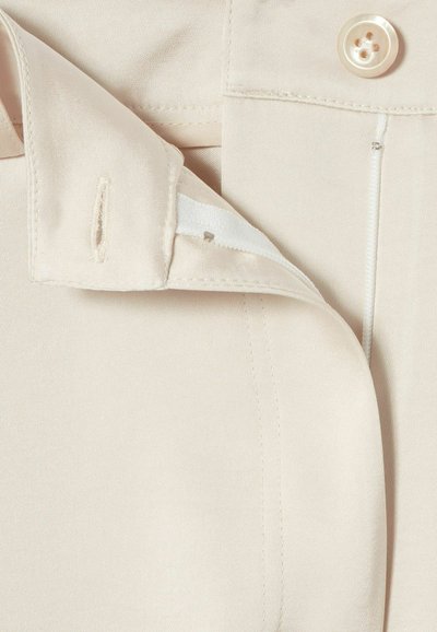 Gros plan sur un tissu beige avec un bouton et un fermoir à scratch partiellement ouvert près d'une boutonnière.