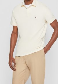 Kortärmad pikétröja i ljus gräddfärgade bomull med avslappnad passform. Har en liten broderad logotyp på bröstet och en klassisk kragsdesign.