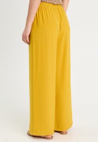Weite Hosen in Senfgelb, aus weichem Stoff gefertigt. Verfügt über einen elastischen Bund und eine glatte Textur, mit einem schlichten, unverzierten Design.