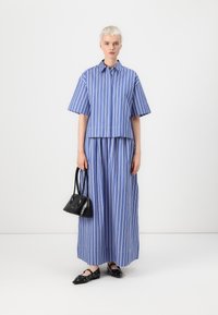 Top a righe verticali blu e bianche e gonna abbinata in cotone, abbinati a una piccola borsa nera e scarpe nere a punta.