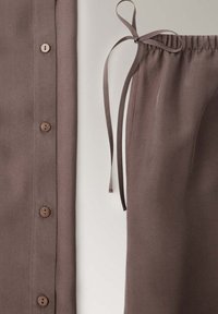 Gros plan sur un vêtement marron boutonné à côté d’un pantalon en tissu marron avec taille élastique et cordon noué.