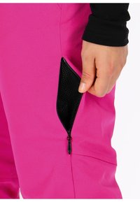 Fuchsia broek met een zwarte ritszak, gladde textuur en taps toelopend ontwerp, met een hand geplaatst nabij de open rits.