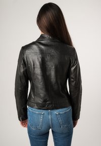 Zwarte leren jas met een slim-fit ontwerp, gestikte details en een klassieke kraag, gecombineerd met blauwe spijkerbroek.