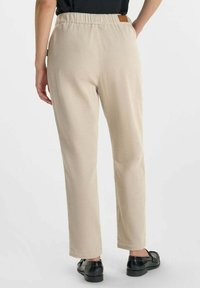 Beige corduroy broek met een recht broekspijpenontwerp, elastische tailleband en een klein leren label op de achterkant. Soepele textuur, minimale details.