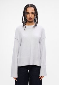 Ανοιχτό γκρι, υπερμεγέθης πλέκτος με ραβδωτά μανίκια και στρίφωμα, με μια μαλακή υφή και χαμηλούς ώμους. Συνδυάζεται με σκούρες τζιν παντελόνες.