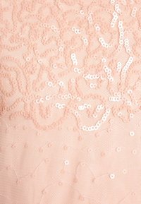 Persikofärgad tyg med intrikata spiraler av paljetter som skapar en texturerad, skimrande yta. Bedårande cirkulär paljettdetaljering genom hela tyget.