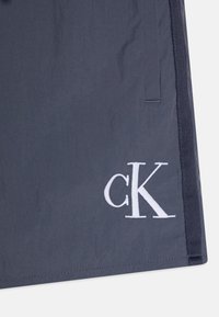 Tamsiai mėlynas audinys, lengvas ir sklandžios tekstūros, su ryškiai balta išsiuvinėta "cK" logotipu apatiniame taške.