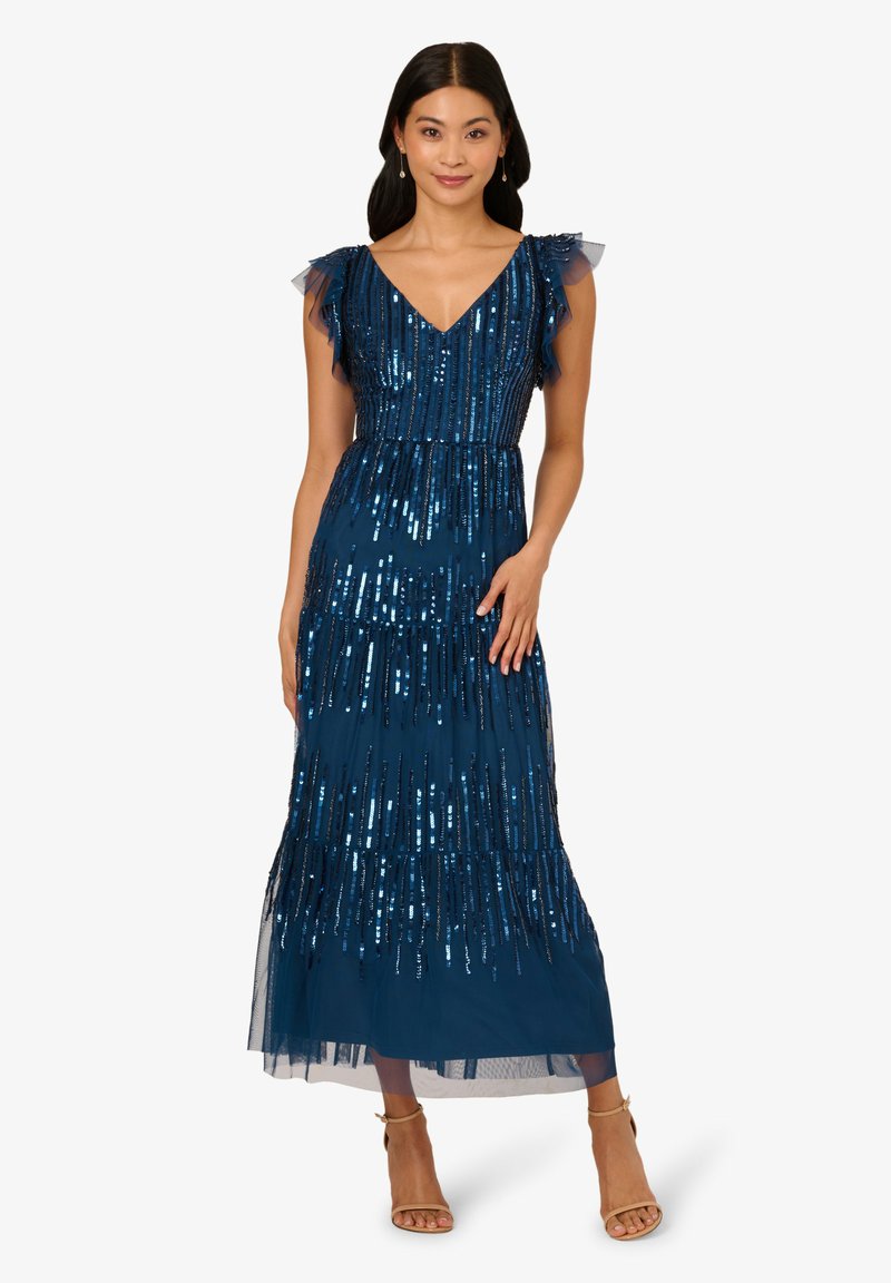 Middengroene glitterjurk met gelaagd ontwerp, V-hals en gekruiste sheer mouwen. Vloerlengte met een aansluitende taille en tule overlay.