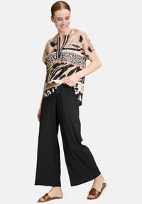 Patroonblouse in beige, zwart en luipaardprint, gecombineerd met zwarte wijde broekspijpen. Bruine sandalen maken de outfit compleet.