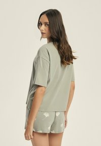 Jasnozielona bawełniana koszulka z krótkim rękawem, zestawiona z pasującymi szortami z wzorem liści w nieco jaśniejszym odcieniu.
