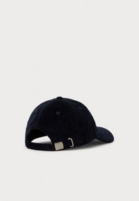 Marineblå kordfløjl baseball cap ligger på hvid overflade, som viser en justerbar metalspænde rem bagpå.