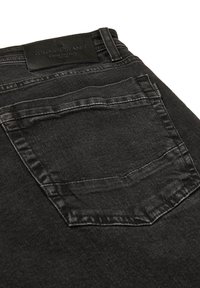 Vaqueros de mezclilla negra con un bolsillo trasero visible, costuras en contraste y una etiqueta de marca de cuero unida a la cinturilla.