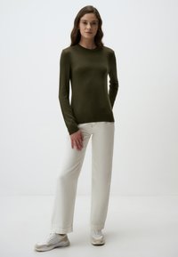 Maglione a maniche lunghe verde scuro con scollatura rotonda, abbinato a pantaloni larghi color avorio e sneaker chiare su uno sfondo neutro.