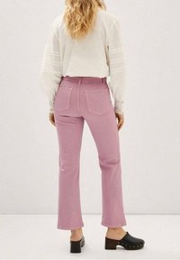 Różowe dzwony z wysokim stanem, z dwiema tylnymi kieszeniami. W zestawieniu z białą bluzką i czarnymi drewnianymi sabotami. Gładka tekstura.