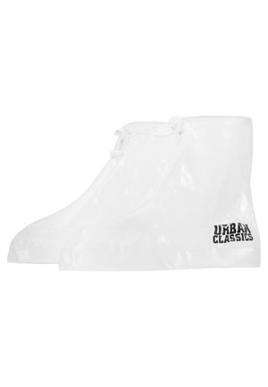 Gjennomsiktige vanntette skooverdeksler med en glatt tekstur, tilpasset design og en svart "URBAN CLASSICS"-logo på siden.
