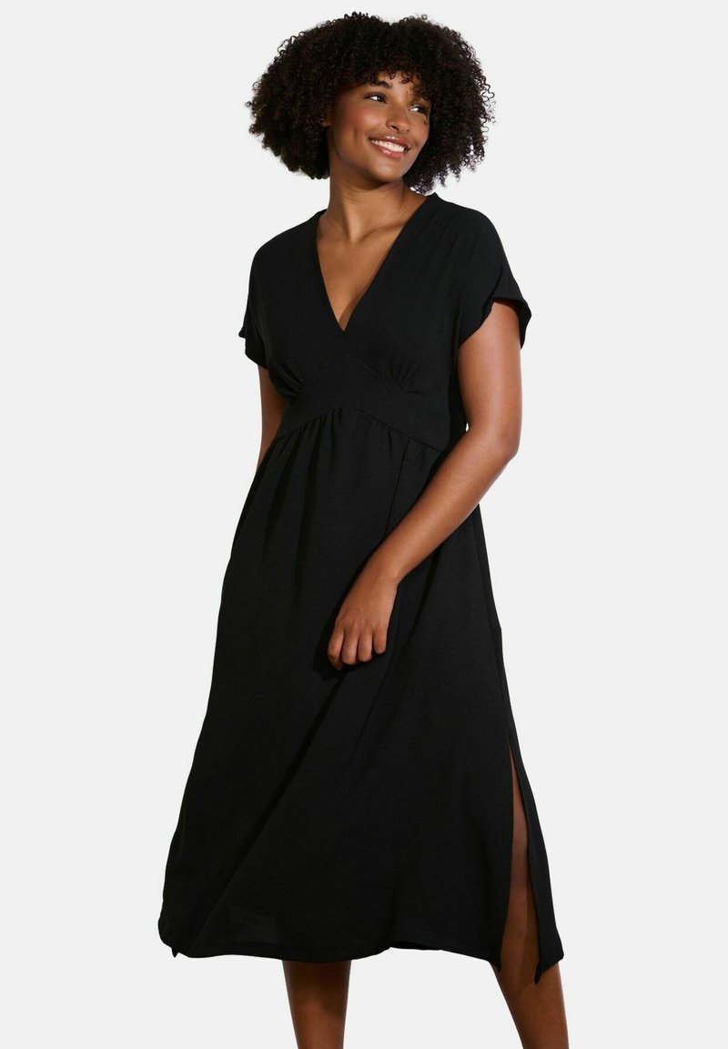 Black midi dress with short sleeves, V-neckline, and empire waist. Features side slits for ease of movement, made from soft fabric.