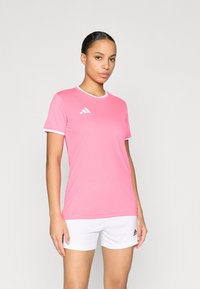 Ροζ αθλητική φανέλα με κοντά μανίκια, λευκό γιακά και λογότυπο με τρεις λευκές ρίγες στο στήθος. Συνδυάζεται με λευκό σορτς. Ομαλή υφή υφάσματος.