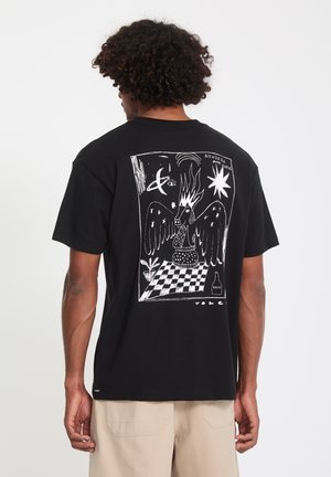 Homme portant un t-shirt noir avec un dessin abstrait blanc d'un cheval ailé, des flammes, des étoiles, une plante et un motif en damier dans le dos.