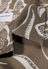 Gros plan d'un col en tissu marron et blanc à motifs avec des coutures visibles et une étiquette de marque floue en arrière-plan.
