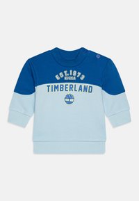 Felpa blu chiaro e blu scuro con maniche lunghe. Presenta il logo e una grafica "TIMBERLAND" sul petto, con dettaglio a bottoni sulla spalla.