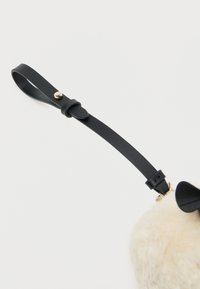 Torba z sztucznego futra o zaokrąglonym kształcie, w kolorze kremowym, z czarnym skórzanym paskiem, złotymi akcentami i odpinanym uchwytem na pasek.