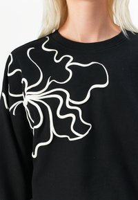 Felpa nera con un grande design bianco ondulato e testurizzato sulla parte frontale, con un collo rotondo e una vestibilità rilassata.