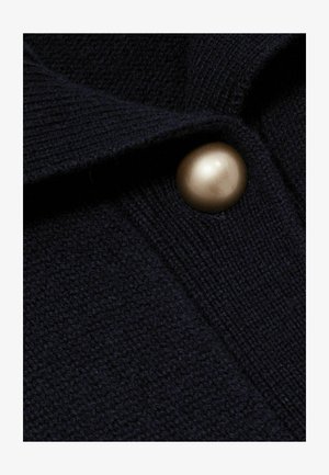 Navyblauer Pullover mit strukturiertem Strick und einem großen, metallisch goldenen Knopf als Akzent. Verfügt über einen subtilen, weichen Stoff.