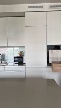 Moderná kuchyňa s lesklými bielymi skrinami, sivým pracovným doskom, mikrovlnnou rúrou a dekoratívnym kvetinovým hrncom s farebným dizajnom.