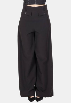 Pantaloni neri a gamba larga con vita alta e due patte frontali abbottonate, indossati con décolleté nere a punta.