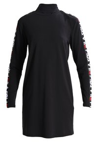 Robe noire à manches longues avec un col montant. Présente des motifs en blanc et rouge le long des manches. Confectionnée dans un tissu lisse et extensible.