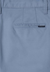 Pantaloni di stoffa azzurro chiaro con una tasca posteriore dotata di un'etichetta nera recante la scritta "HACKETT". Tessuto liscio con un design semplice.
