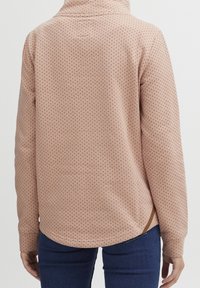 Top rosa chiaro a maniche lunghe con piccoli pois color bordeaux, orlo arrotondato, spacchi laterali e colletto alto. Tessuto morbido.