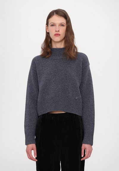 Mørk grå cropped sweater med ribkant ved halsudskæringen og kanten, med lange ærmer og en blød strikket tekstur. Sorte fløjl bukser komplimenterer looket.