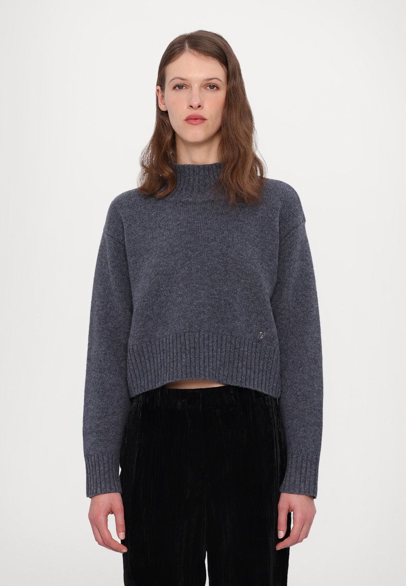 Pull court gris foncé avec un col et un ourlet côtelés, doté de manches longues et d'une texture tricotée douce. Un pantalon en velours côtelé noir complète le look.