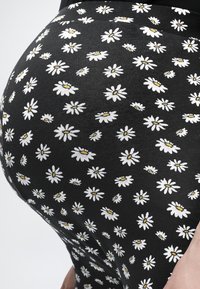 Gros plan sur un legging noir avec un motif marguerite blanc et jaune porté sur la hanche et la cuisse d'une personne.