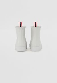 Bottes de cheville blanches en caoutchouc avec surface texturée et semelle blanche, dotées de languettes de tirage rouges, noires et blanches à l'arrière.