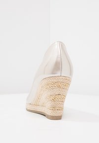 Chaussure à talon en coin argent métallique avec une base texturée ressemblant à de la paille. Bout pointu et surface supérieure lisse et réfléchissante.