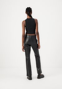 Black cropped tank top paired with high-waisted black faux leather pants and chunky black footwear. Smooth texture, minimal design.