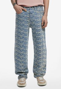 Blå og crème farvede denim bukser med mønster, løs pasform, med en tekstureret overflade. Har lommer og en waistband. Sættes sammen med lyse sneakers.