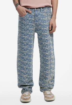 Blue and cream patterned denim pants, loose fit, with a textured surface. Features pockets and a waistband. Paired with light sneakers.
