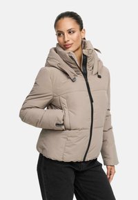 Beige puffjacka med hög krage och justerbar huva, med en svart dragkedja och manschetter. Slät textur med synliga sömnadsdetaljer.