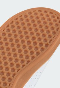 Suela de zapatilla blanca con un patrón de panal y un borde de goma marrón. Textura suave con pequeñas perforaciones a lo largo del borde.