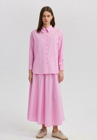 Růžová košile s dlouhými rukávy a knoflíkovou chipou, doplněná o odpovídající růžovou maxi sukni. Měkký materiál s hladkou texturou.