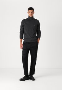 Maglione collo alto grigio scuro abbinato a pantaloni neri. Il maglione presenta polsini e orlo a coste, mentre i pantaloni hanno una vestibilità dritta. Scarpe nere completano il look.