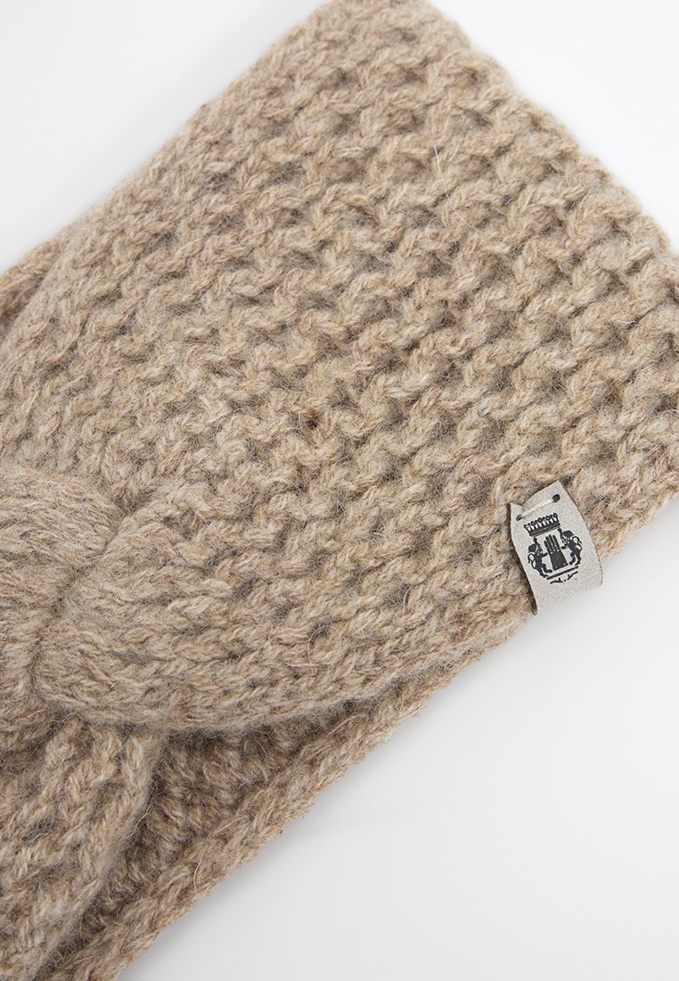 Beige gestricktes Wollhaarband mit gedrehtem Knoten und kleinem weißen Etikett mit schwarzem Emblem auf weißem Hintergrund.