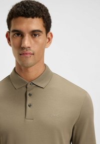 Beige polo shirt met een kraag en drie zwarte knopen, met een subtiele geborduurde "BOSS" logo op de linkerborst.