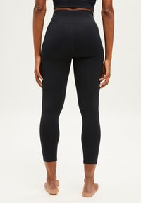 Leggings noires taille haute avec un design ajusté, texture lisse et longueur cropped, dotés de coutures renforcées et sans logos visibles.