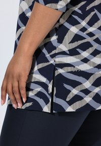 Top di colore navy con motivi astratti a strisce grigio chiaro e bianche, con spacchi laterali all'orlo e una vestibilità morbida. Tessuto morbido e confortevole.